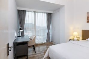 A hotel room with a bed, desk, chair, and a view through large windows.