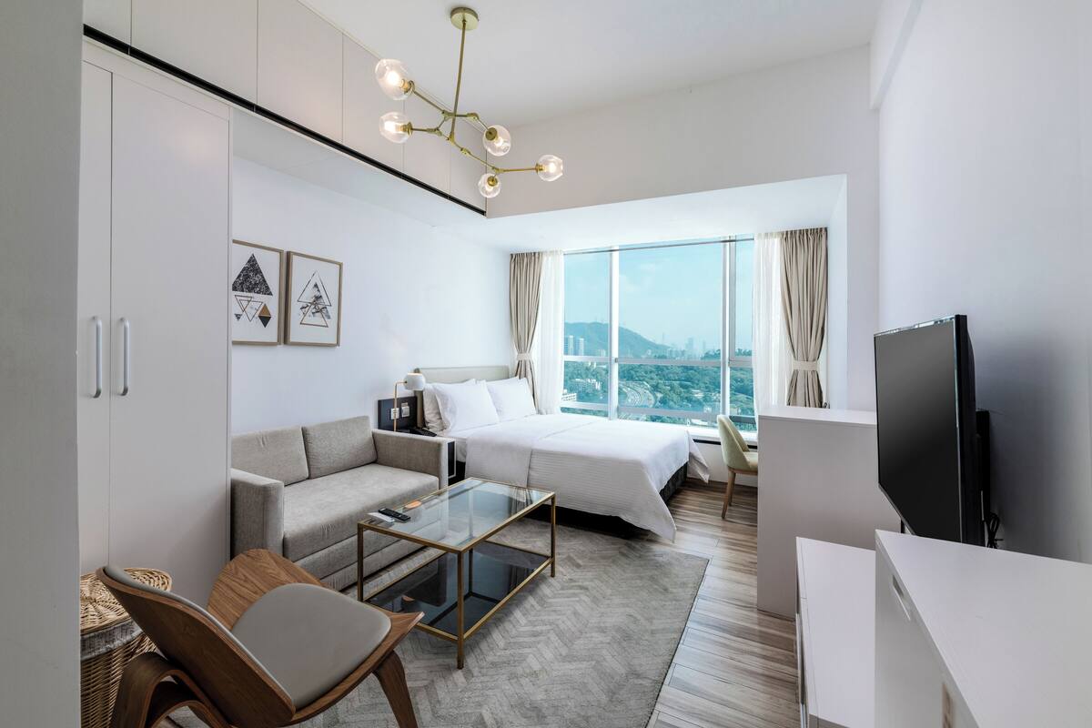 Ein modernes Hotelzimmer mit Bett, Sofa, Fernseher und Blick auf die Stadt.