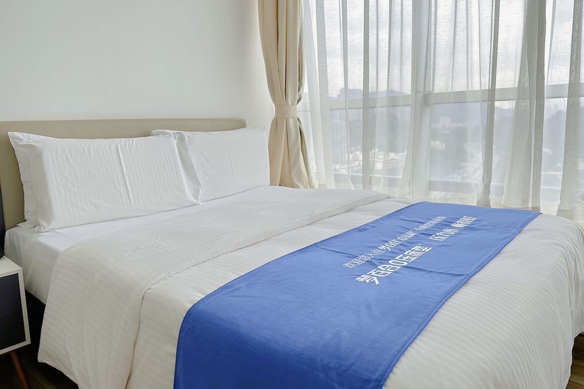 Ein Hotelzimmer mit Bett, weißer Bettwäsche und einer blauen Tagesdecke mit Schriftzug.