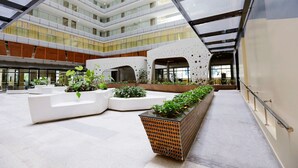 Un atrio amplio con varios niveles, zonas de estar modernas y una jardinera central con follaje.