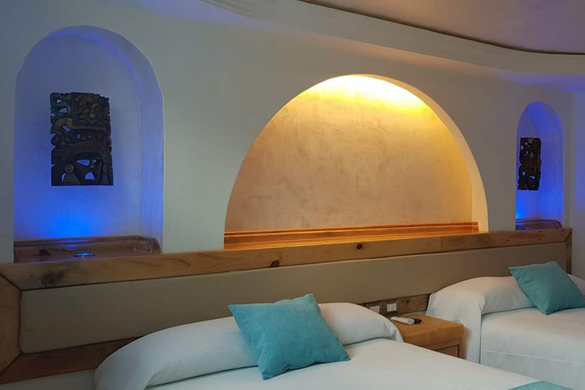 Ein Hotelzimmer mit zwei Betten, einem Holzkopfteil und einem großen, bogenförmigen Fenster mit einer Lampe.