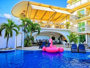 A pool area with a pink inflatable flamingo, lounge chairs, and a covered seating area with tables and chairs. - Hotel Blue Star Cancun (Cancun)