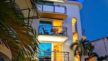 Un immeuble à plusieurs étages doté de balcons, d’un espace extérieur aménagé pour s’asseoir et de palmiers.