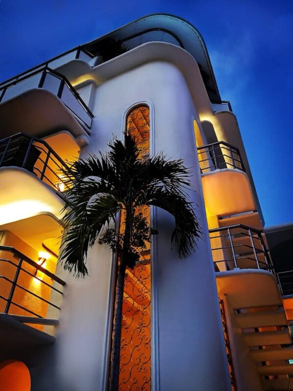 A modern building with a curved facade, a central vertical window with a decorative pattern, and balconies with railings. - Hotel Blue Star Cancun (Cancun)