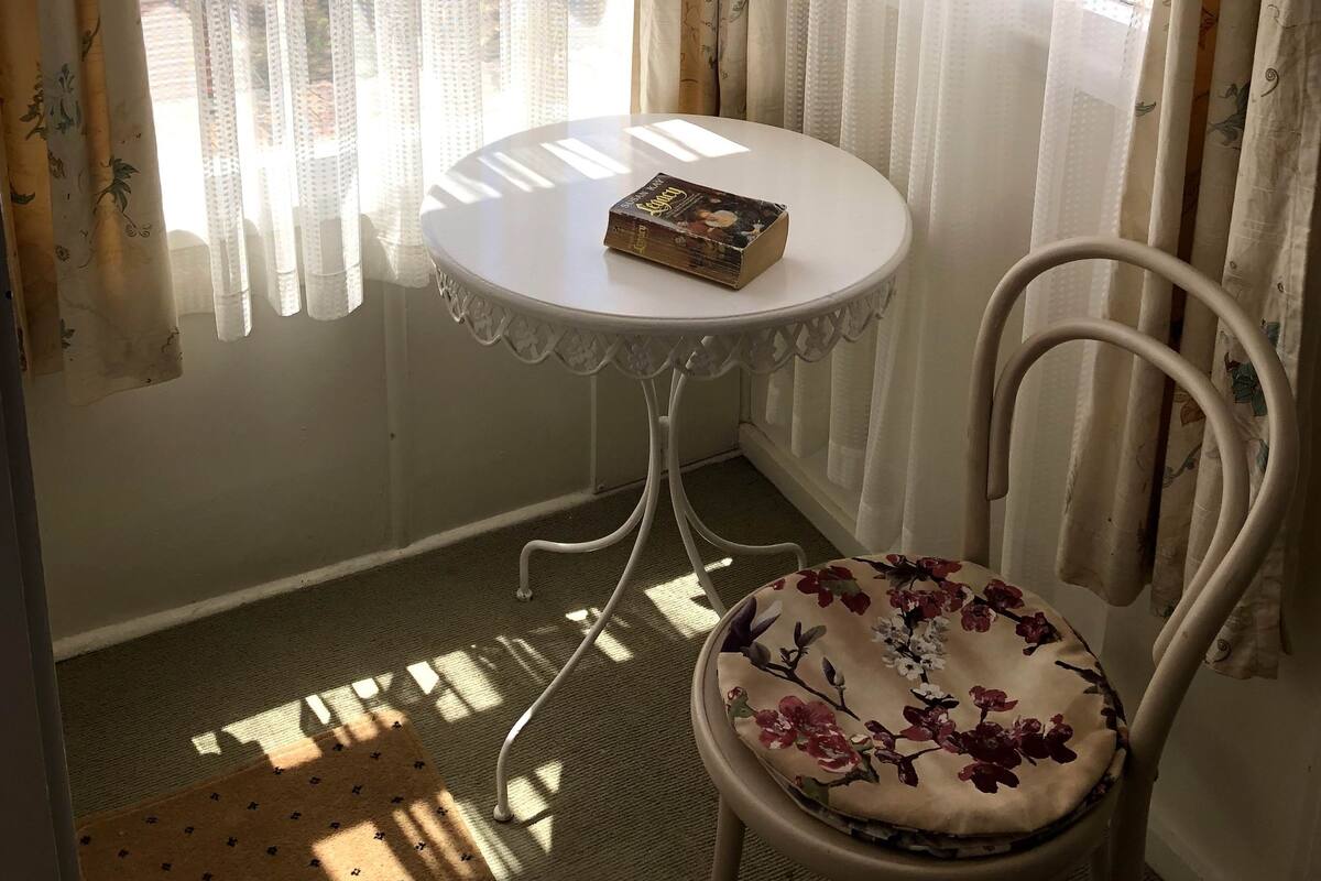 A corner room with a small round table, a chair, and a book on the table.
