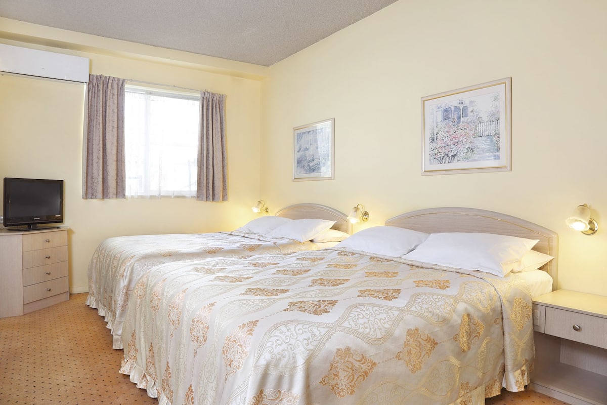 A hotel room with two beds, a television, a dresser, and artwork on the walls.
