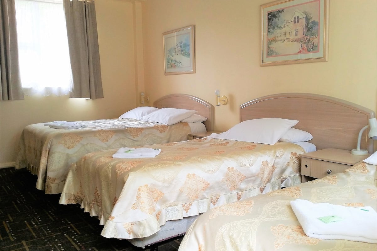 A hotel room with two beds, a window with curtains, and two framed pictures on the wall.