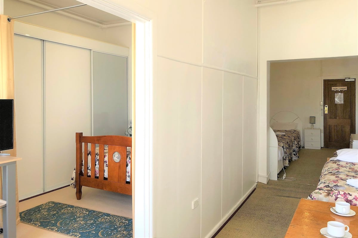 A hotel room with a bed, a wooden chair, a small table with cups, a mirror, and a wardrobe.