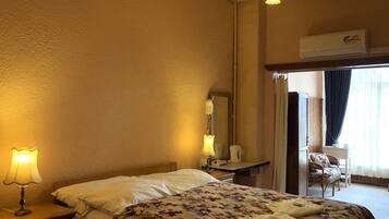 A hotel room with a bed, bedside lamp, mirror, and a chair by the window.