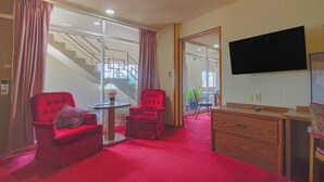 A hotel room with a red carpet, two red armchairs, a wooden dresser, a flat-screen TV, and a staircase leading to an outdoor area. - HomeTown Inn by OYO - Liberal, KS (Liberal)