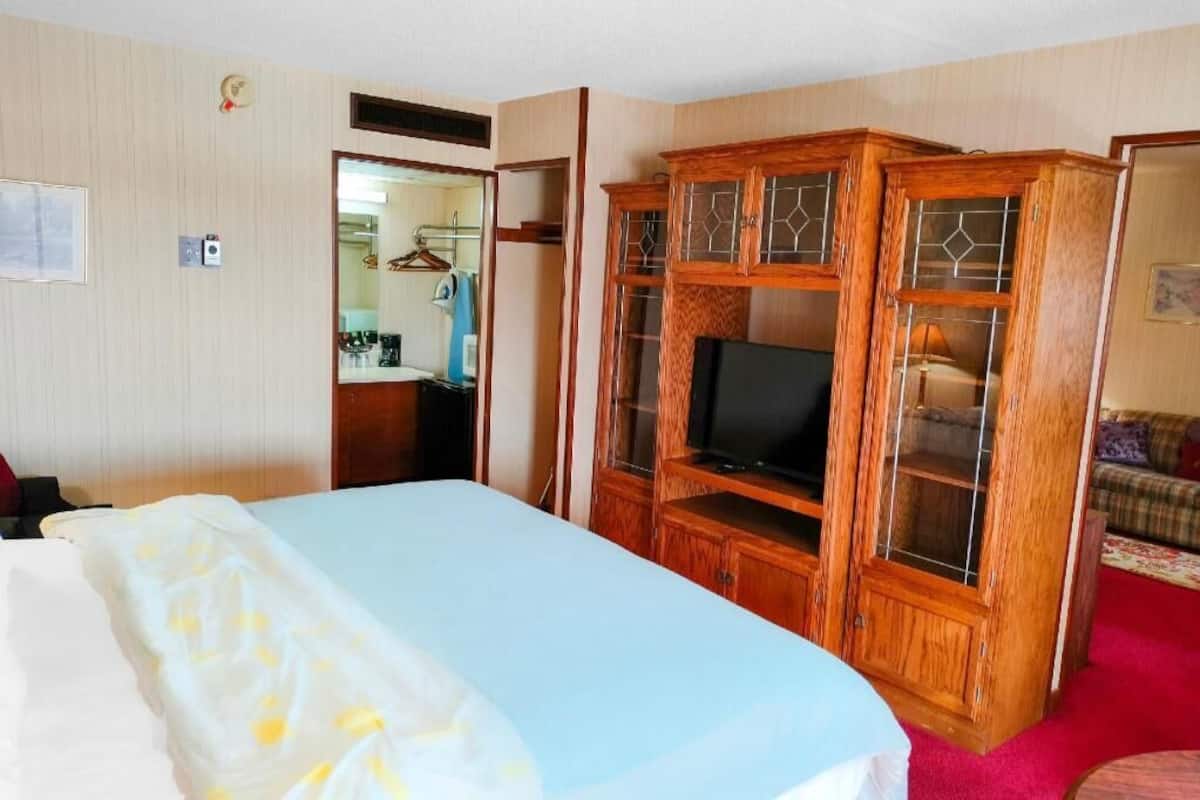 A hotel room with a bed, a wooden TV stand, a wardrobe, and a red carpet.