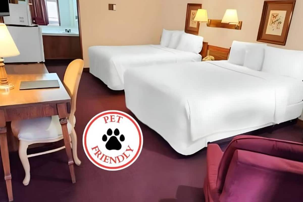 A hotel room with two beds, a desk, a chair, and a small table.