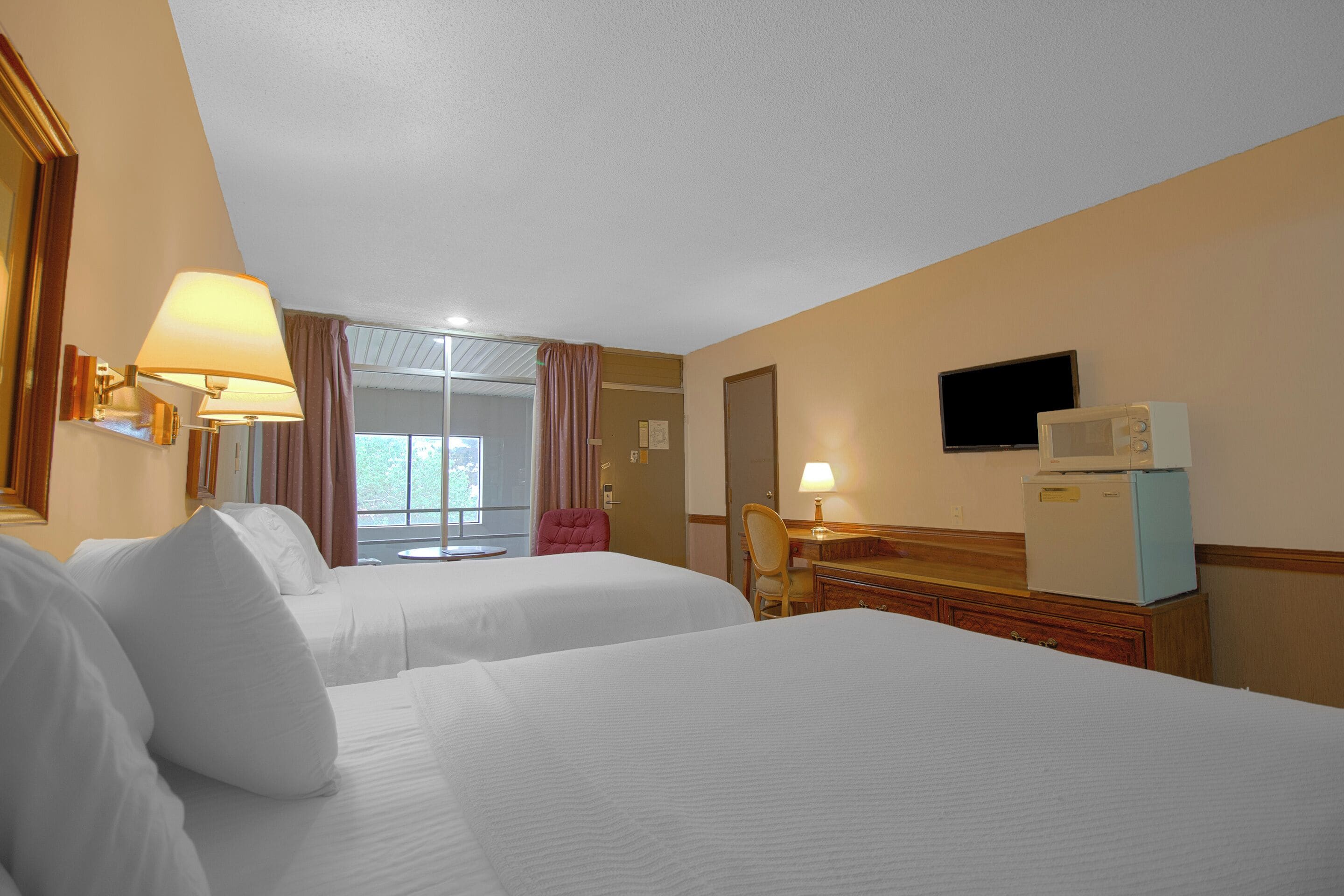 Ein Hotelzimmer mit zwei Betten, einem Schreibtisch, einem Sessel, einem Fernseher und einem Kühlschrank.