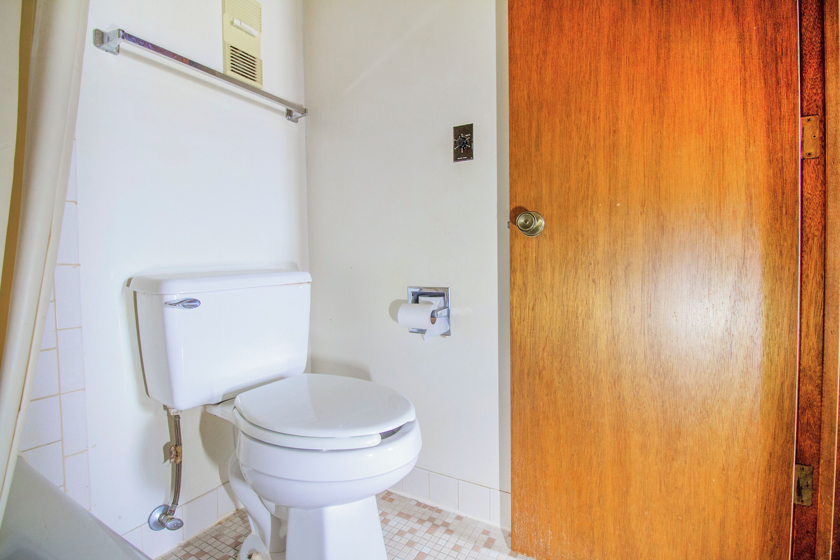 A bathroom with a white toilet, a wooden door, and a towel rack.