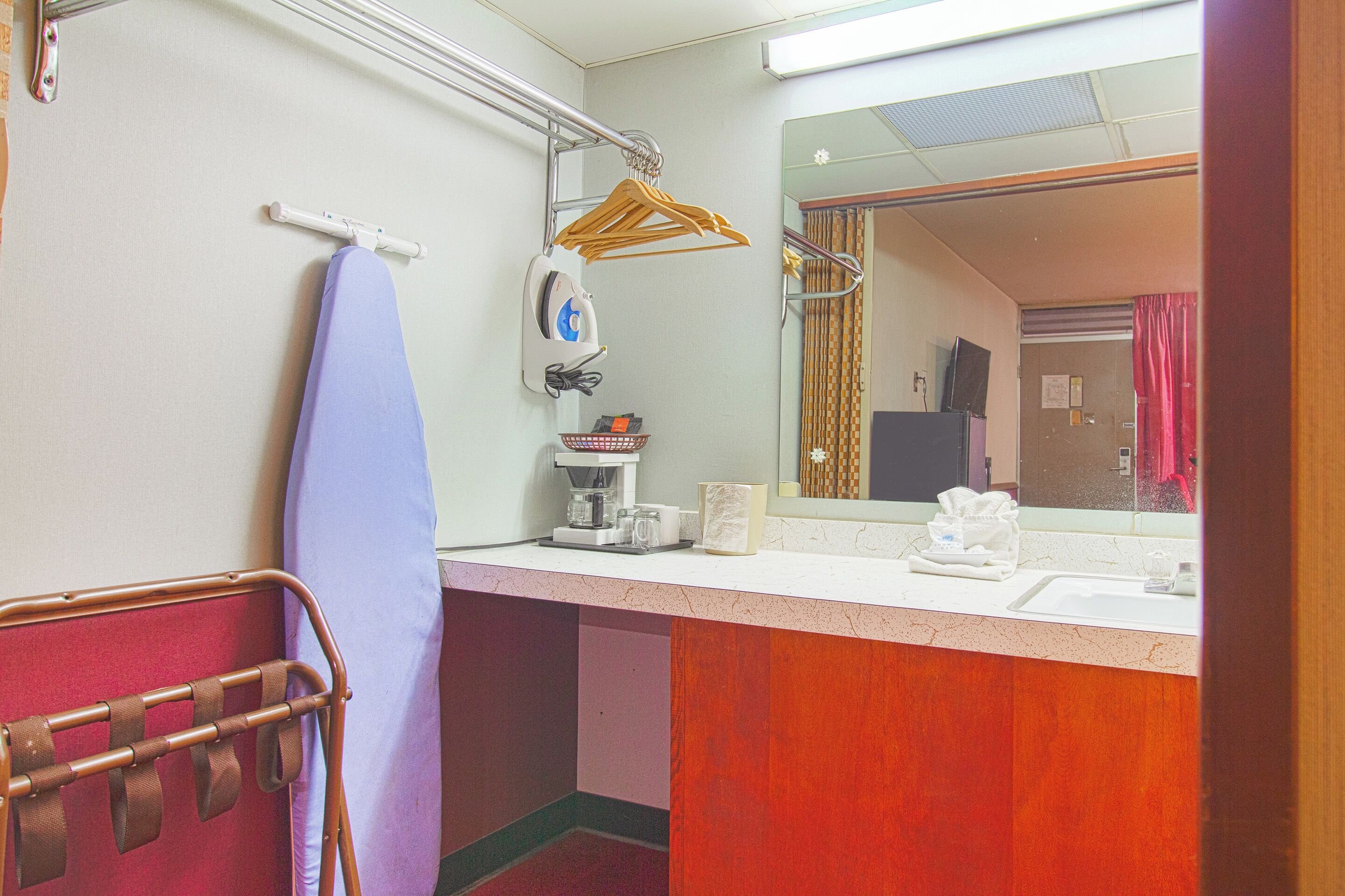 A bathroom with a sink, mirror, towel rack, and a hanging clothes rack.