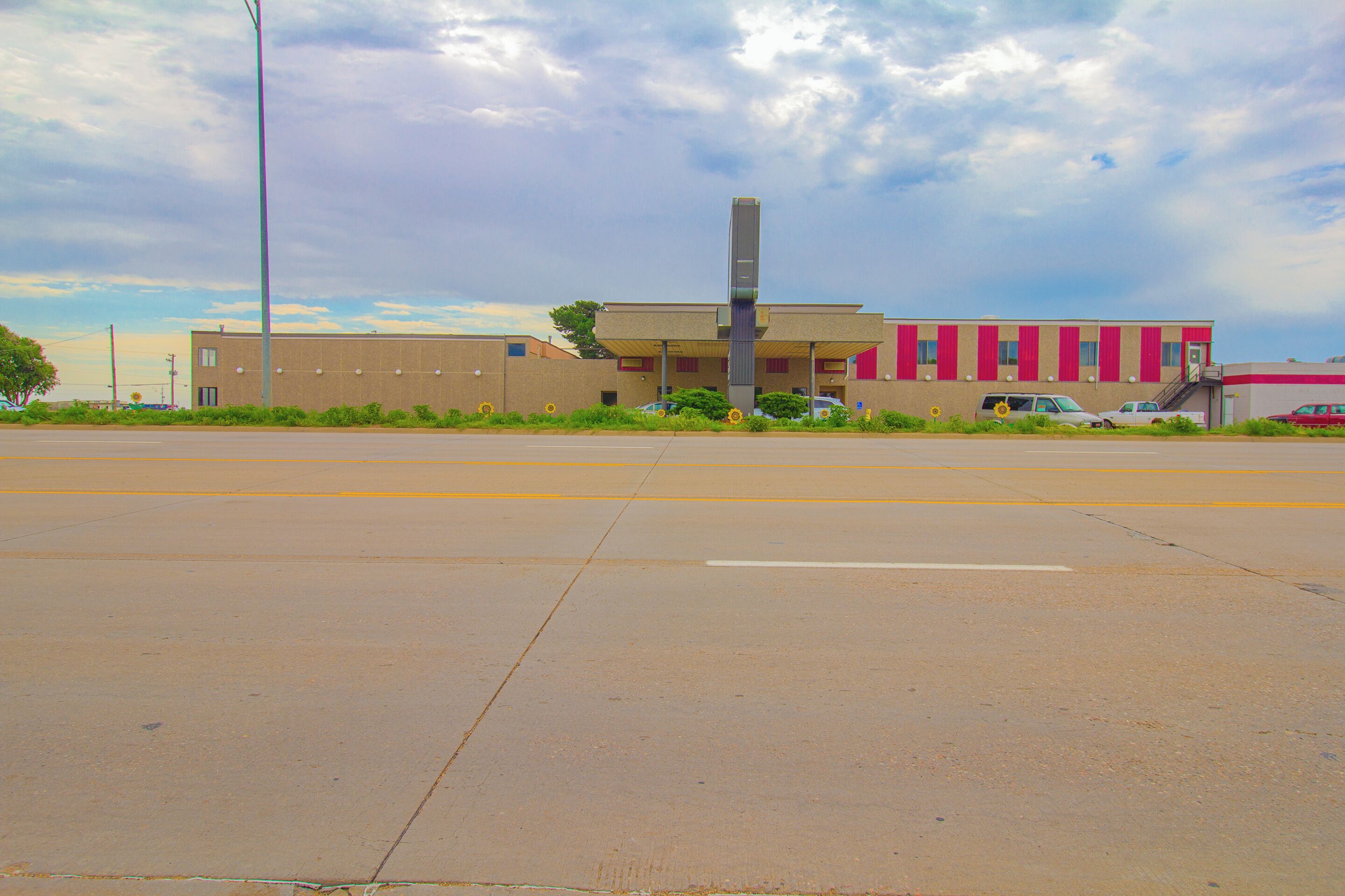 A building with a flat roof, a central vertical structure, and a parking lot in front.