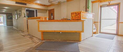 A reception area with a wooden reception desk, a mat at the entrance, and a hallway with wooden flooring.