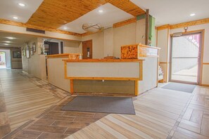 A reception area with a wooden reception desk, a mat at the entrance, and a hallway with wooden flooring.