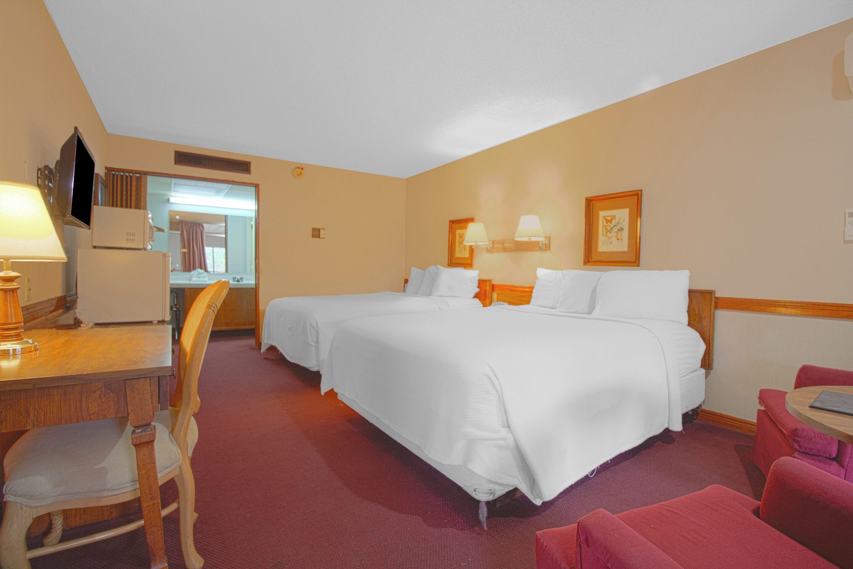 Une chambre d’hôtel avec deux lits, un bureau avec une lampe, une chaise et une petite table.