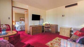 Ein Hotelzimmer mit rotem Teppich, einem Bett mit weißer Bettdecke, einem Holztisch, einem Stuhl, einem an der Wand montierten Fernseher und einem kleinen Schrank.