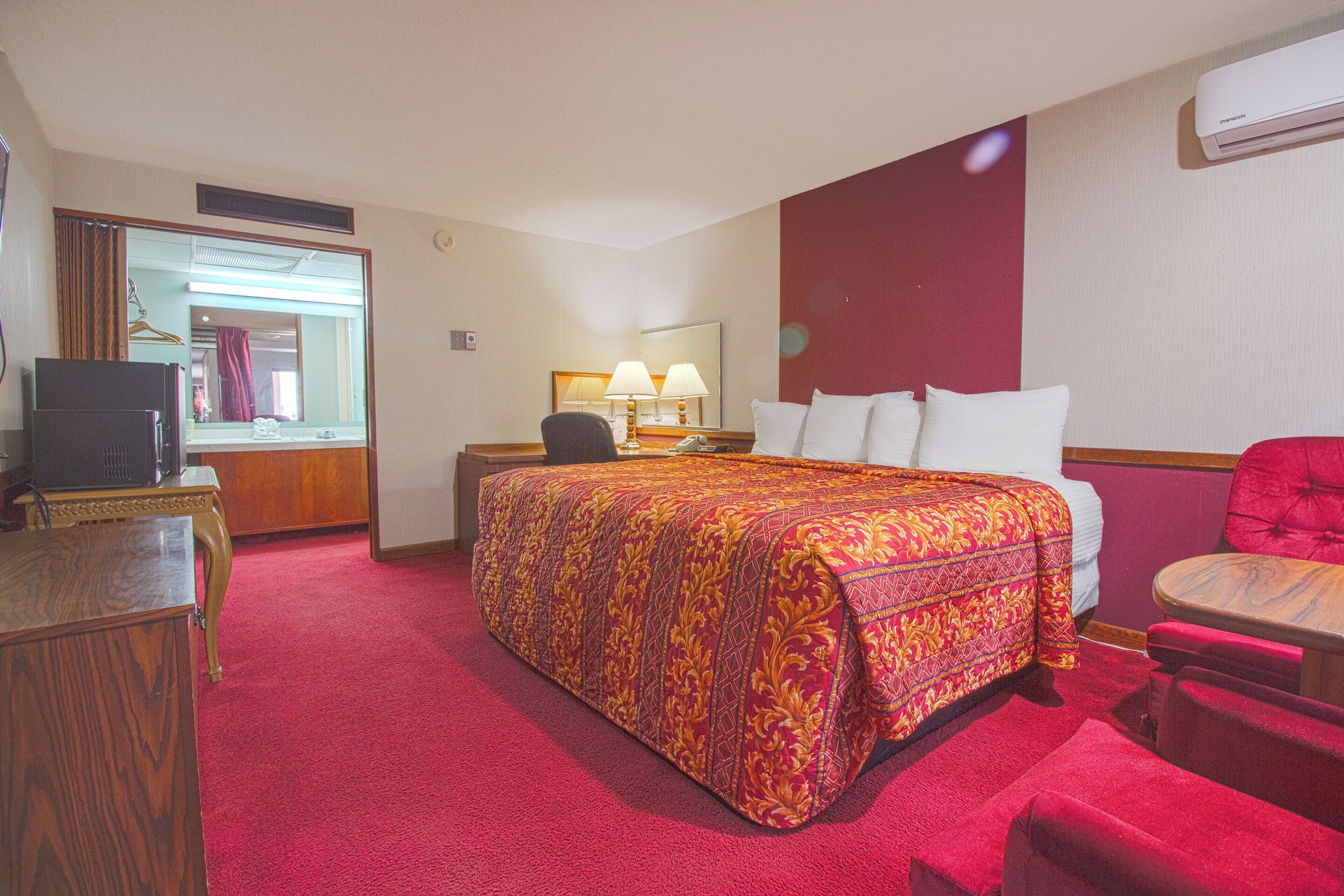 A hotel room with a large bed, a desk with a computer, a chair, and a red carpet.