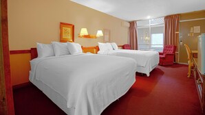 A hotel room with two beds, a red carpet, a wooden headboard, a red armchair, and a desk with a lamp. - HomeTown Inn by OYO - Liberal, KS (Liberal)