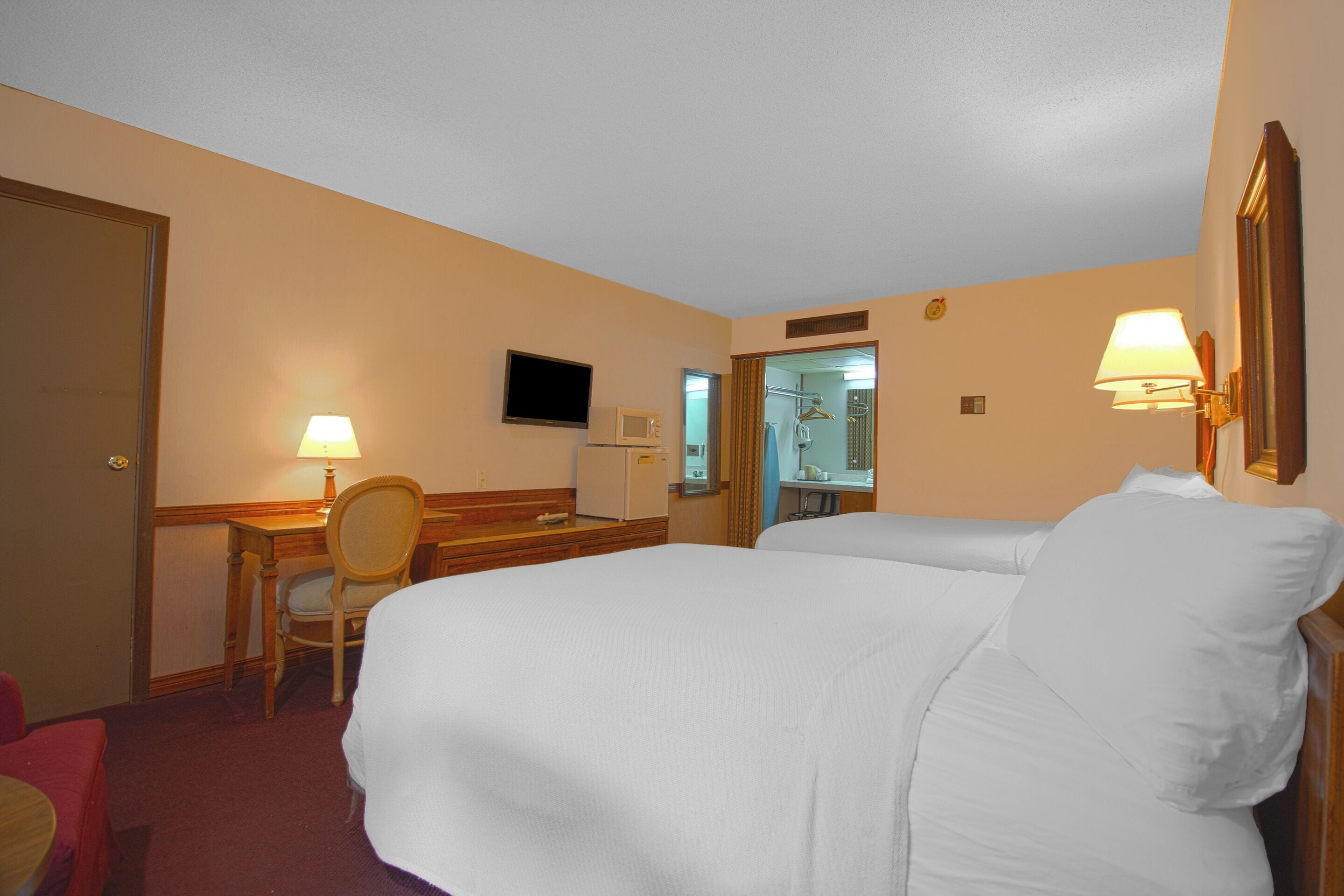 Une chambre d’hôtel comprenant un lit, un bureau avec une chaise, une télévision et un miroir.