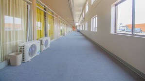 A long corridor with air conditioning units lined up on one side, large windows on the other, and a view of the outside through the windows. - HomeTown Inn by OYO - Liberal, KS (Liberal)