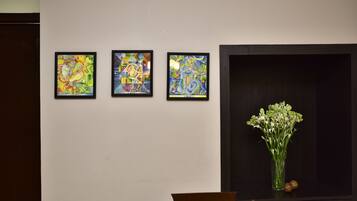 A wall with three framed abstract paintings and a vase with flowers on a cabinet.