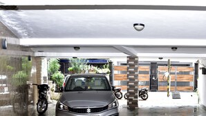 A covered parking area with a car and motorcycles, a security camera, and a gated entrance. - Woodpecker - 2 Bedroom Service Apartment (New Delhi)
