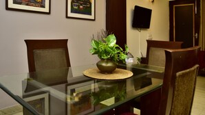 A dining table with chairs, a vase with a plant, framed artwork on the wall, and a television on the wall. - Woodpecker - 2 Bedroom Service Apartment (New Delhi)