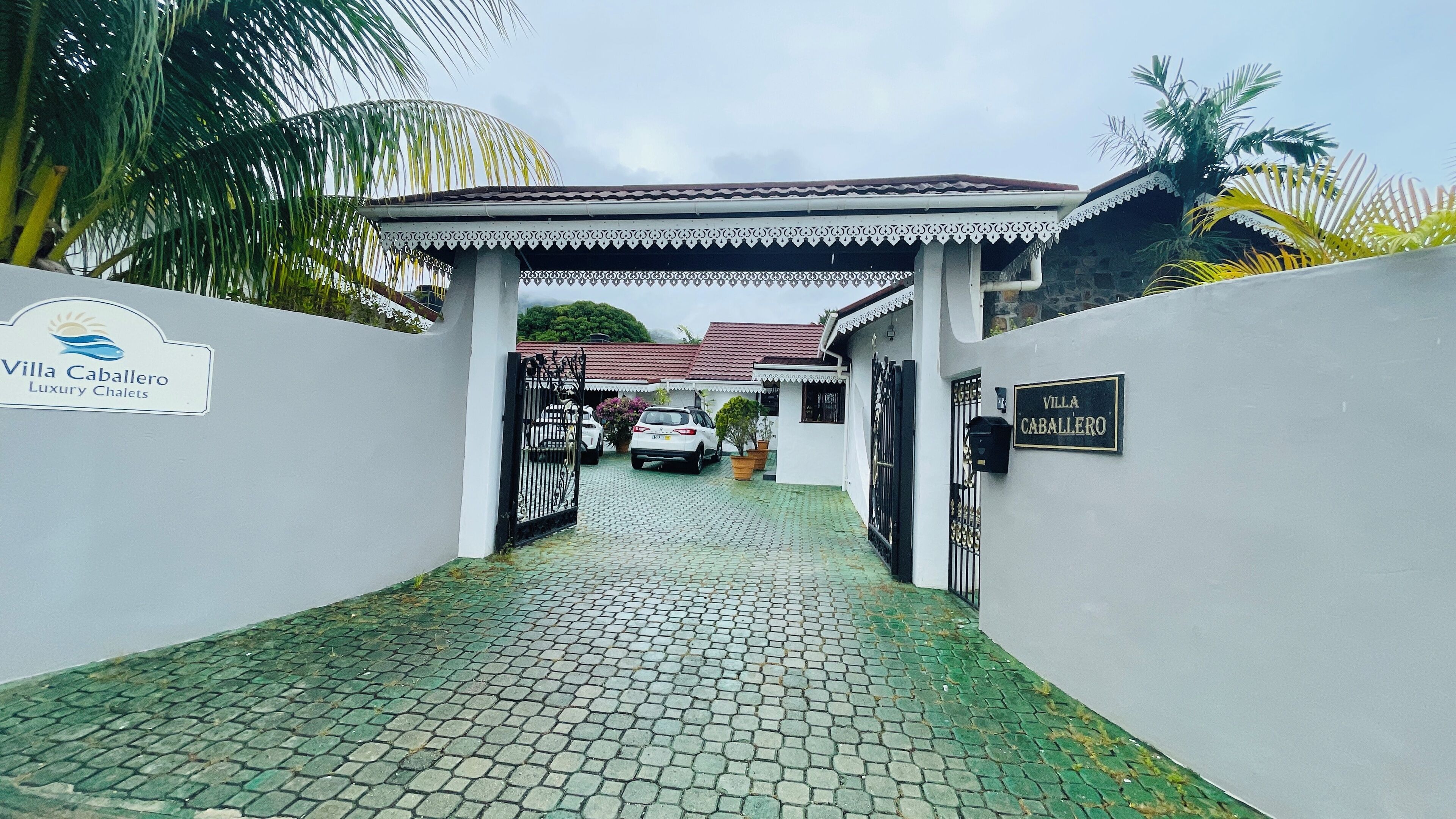 A gated entrance to a property named Villa Caballero, featuring a paved pathway leading to a covered area with a tiled roof.