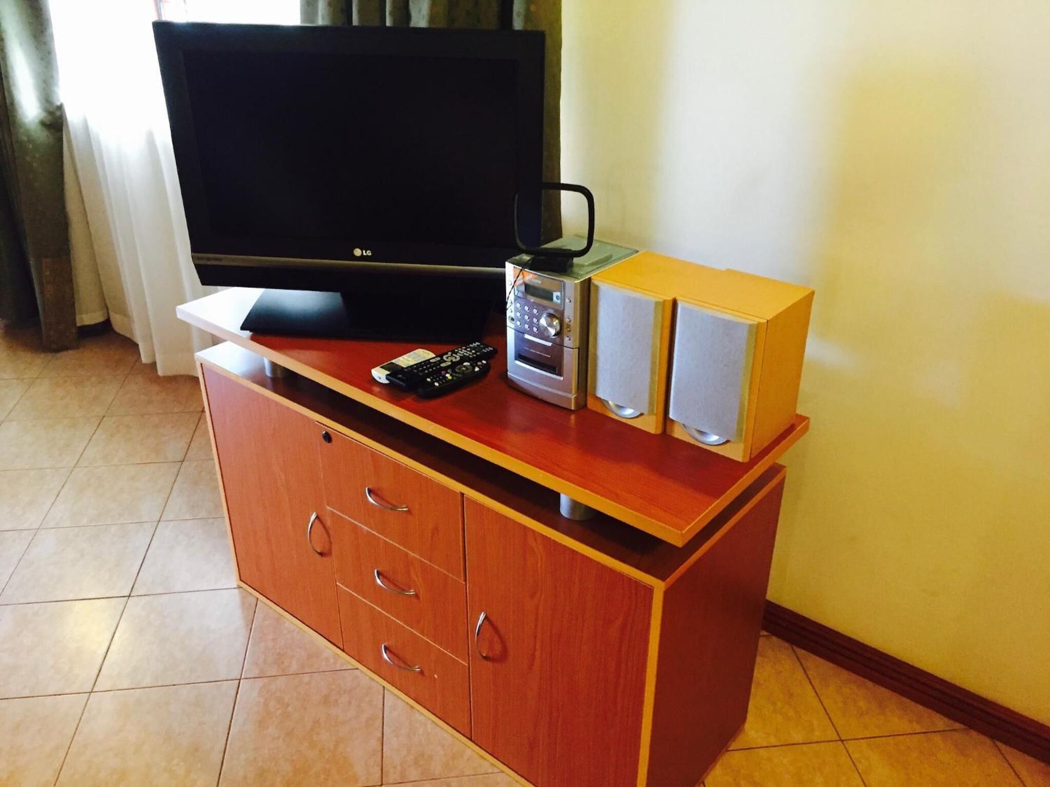 A wooden entertainment unit with a flat-screen TV, a radio, and two speakers.