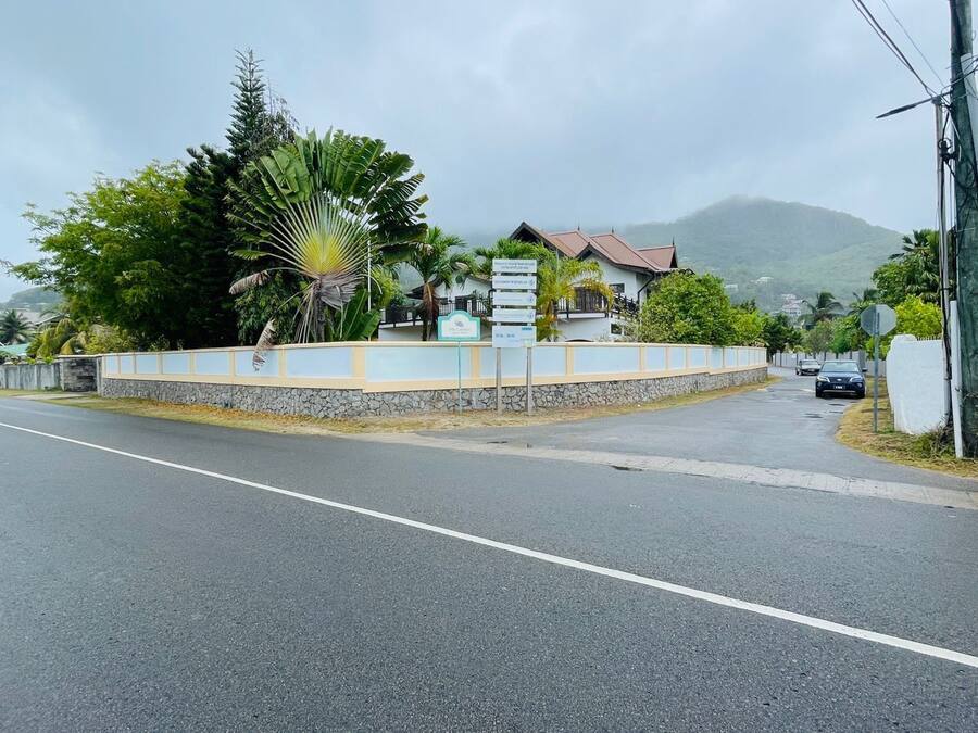 Una carretera que conduce a un edificio con un muro de piedra y un cartel.