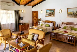 Habitación de hotel con cama, dos sofás, escritorio, televisor y obras de arte en las paredes.
