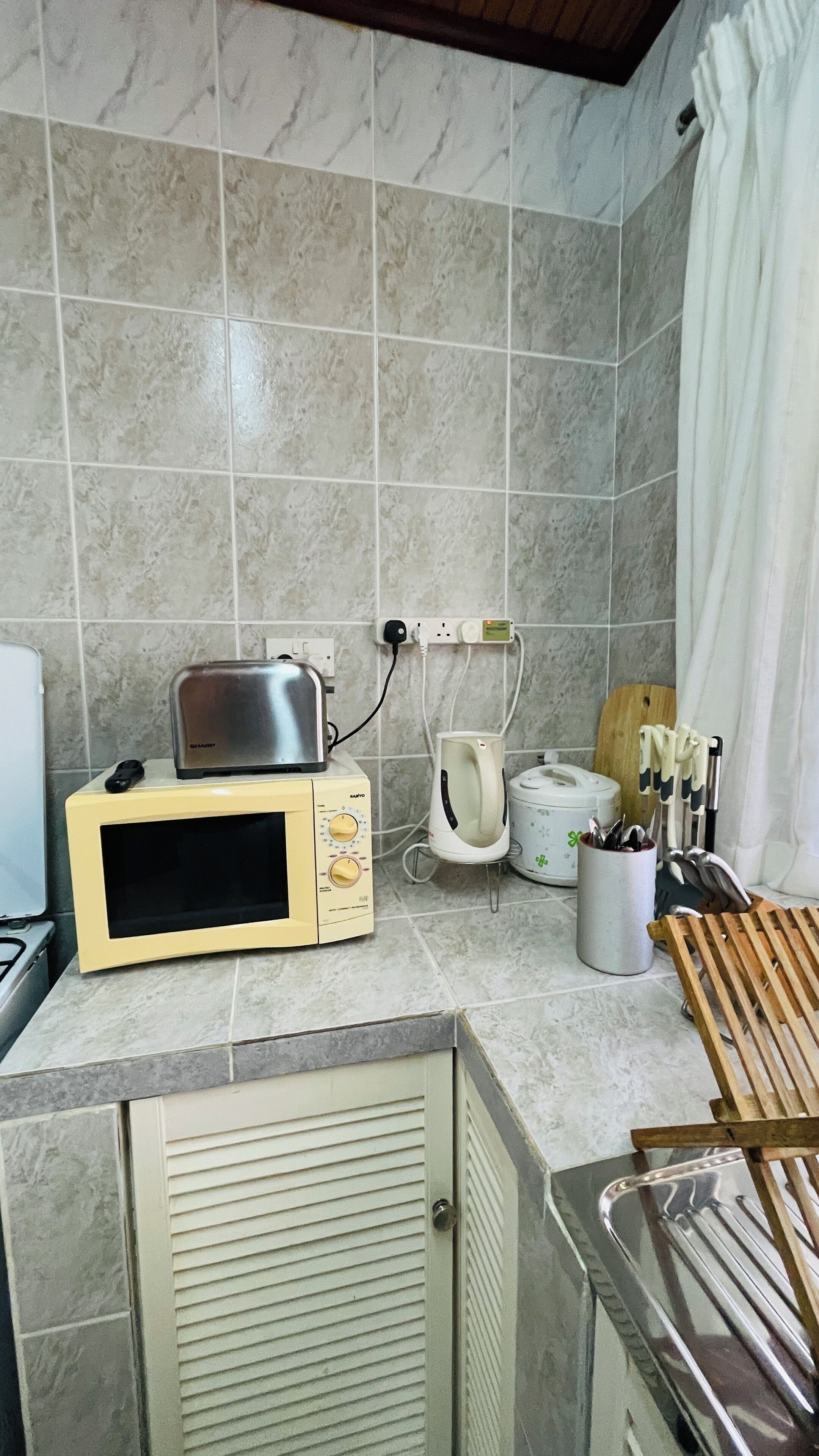 A kitchen with a microwave, toaster, kettle, and a wooden cutting board.