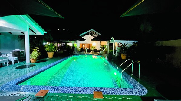 A nighttime swimming pool with tiled edges, surrounded by lounge chairs and potted plants. - Villa Caballero Luxury Chalets (Mahé Island)