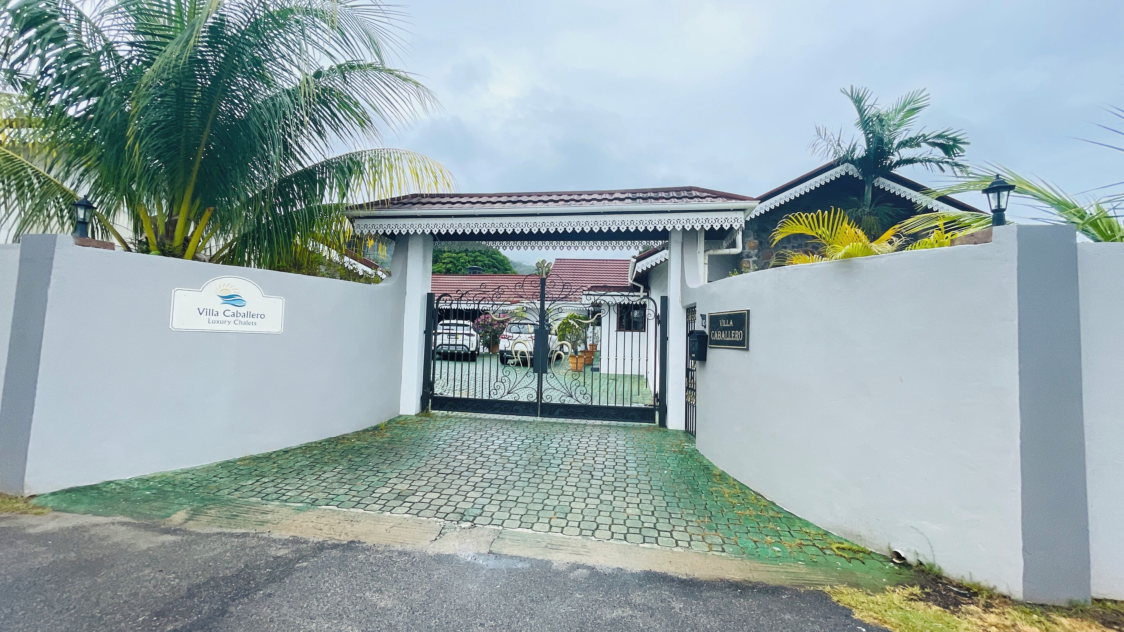 Une entrée fermée par un portail mène à une propriété appelée Villa Caballero, qui se caractérise par une allée pavée et un portail décoratif.