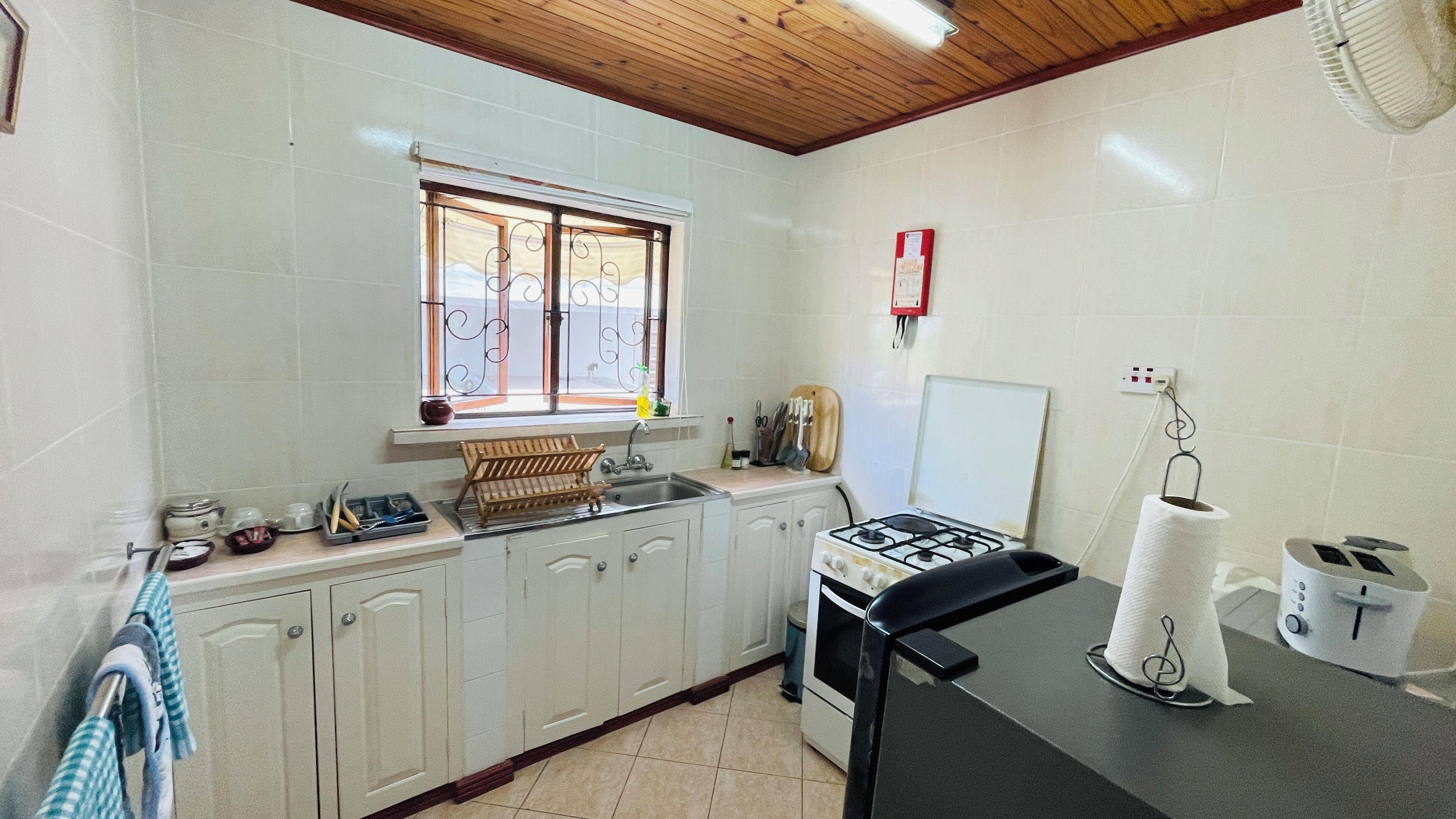 Una cucina con mobili bianchi, piano cottura a gas, lavello e finestra vista edificio.