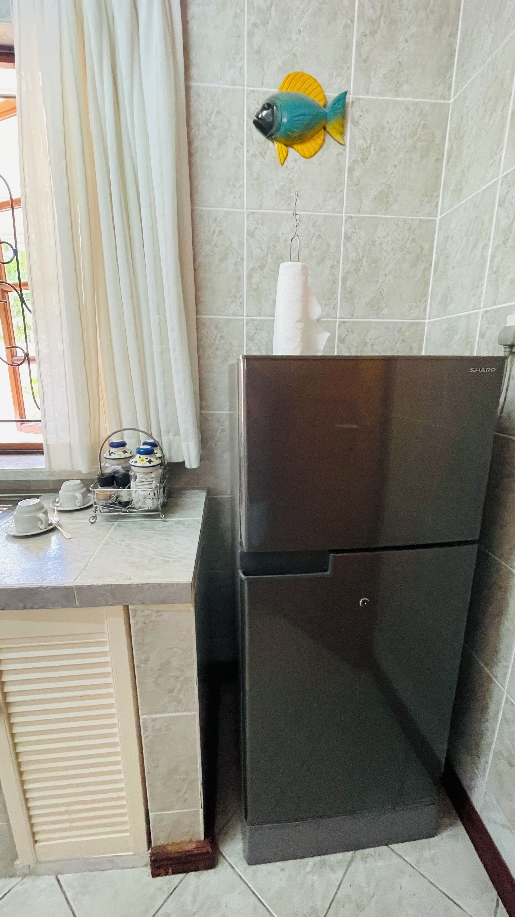 Una cocina con un refrigerador, una ventana con cortinas y una decoración de pescado en la pared.