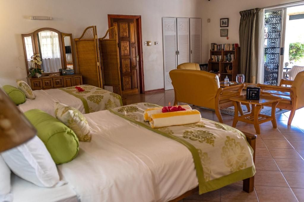 A hotel room with two beds, a sitting area with a table and chairs, a bookshelf, and a wardrobe.
