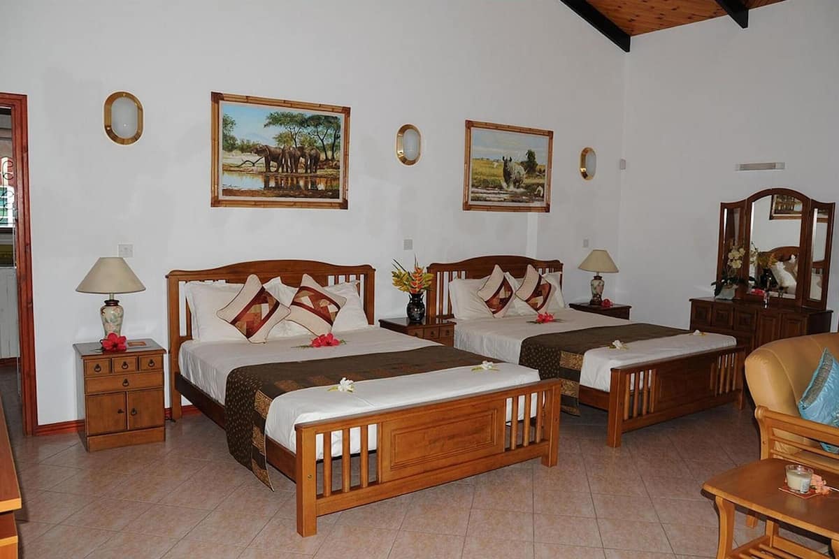 A hotel room with two wooden beds, each with a nightstand, a lamp, and a mirror. There are framed pictures on the wall and a wooden chair in the corner.