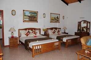 A hotel room with two wooden beds, each with a nightstand, a lamp, and a mirror. There are framed pictures on the wall and a wooden chair in the corner. - Villa Caballero Luxury Chalets (Mahé Island)