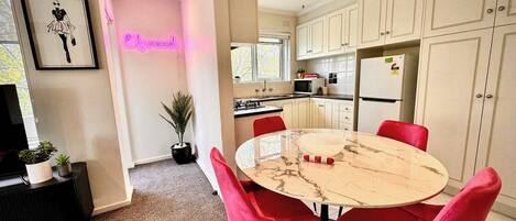 Una cocina moderna con armarios blancos, una mesa redonda de mármol y sillas rojas.