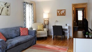 Un salón con un sofá gris, un sillón beis, un escritorio y una mesita con plantas.