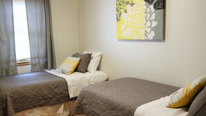 Un dormitorio con dos camas, cada una con colcha marrón acolchada y ropa de cama blanca. Hay una obra de arte floral en la pared sobre las camas.
