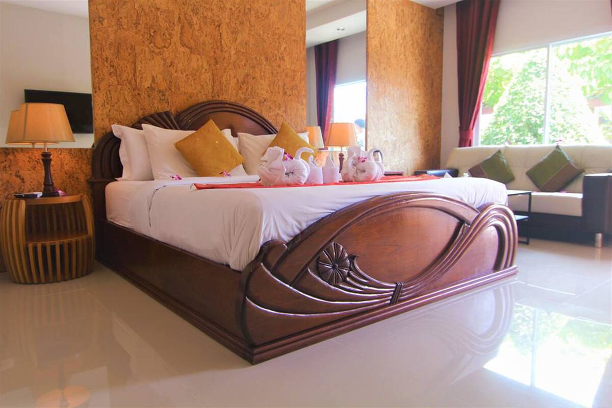 Habitación de hotel espaciosa con una cama grande, un sofá y un ventanal con vistas a zonas verdes.