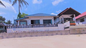 Una propiedad frente al mar con una casa grande que tiene un balcón, un área de piscina con sillas de descanso y un muro de concreto al frente.