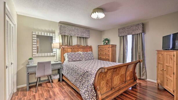 Un dormitorio con una cama de madera, un escritorio con silla, un aparador, un televisor y un espejo.