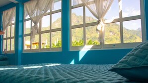 Un dormitorio con cama, cortinas y vistas a montañas a través de amplios ventanales.
